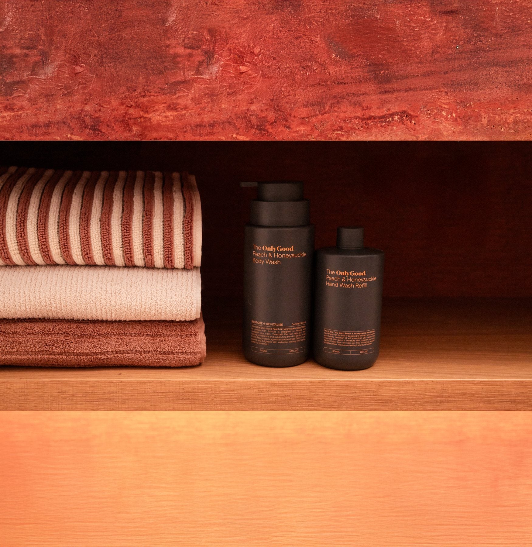 Only Good® Peach & Honeysuckle hand and body wash on a red shelf beside folded striped towels.