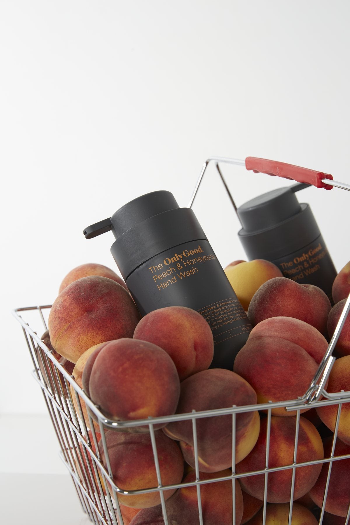 Only Good® Peach & Honeysuckle in a wire basket full of peaches.