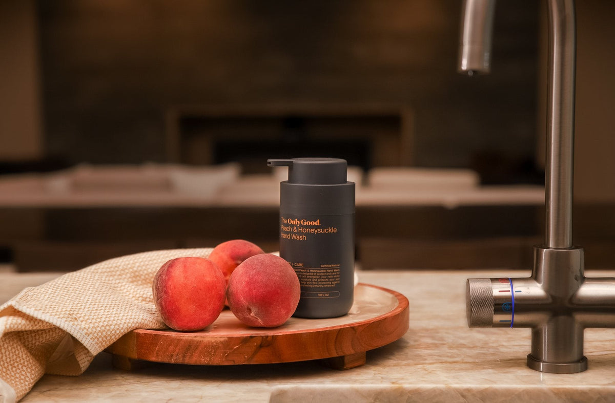 Only Good Peach and Honeysuckle hand wash at a kitchen sink beside peaches.