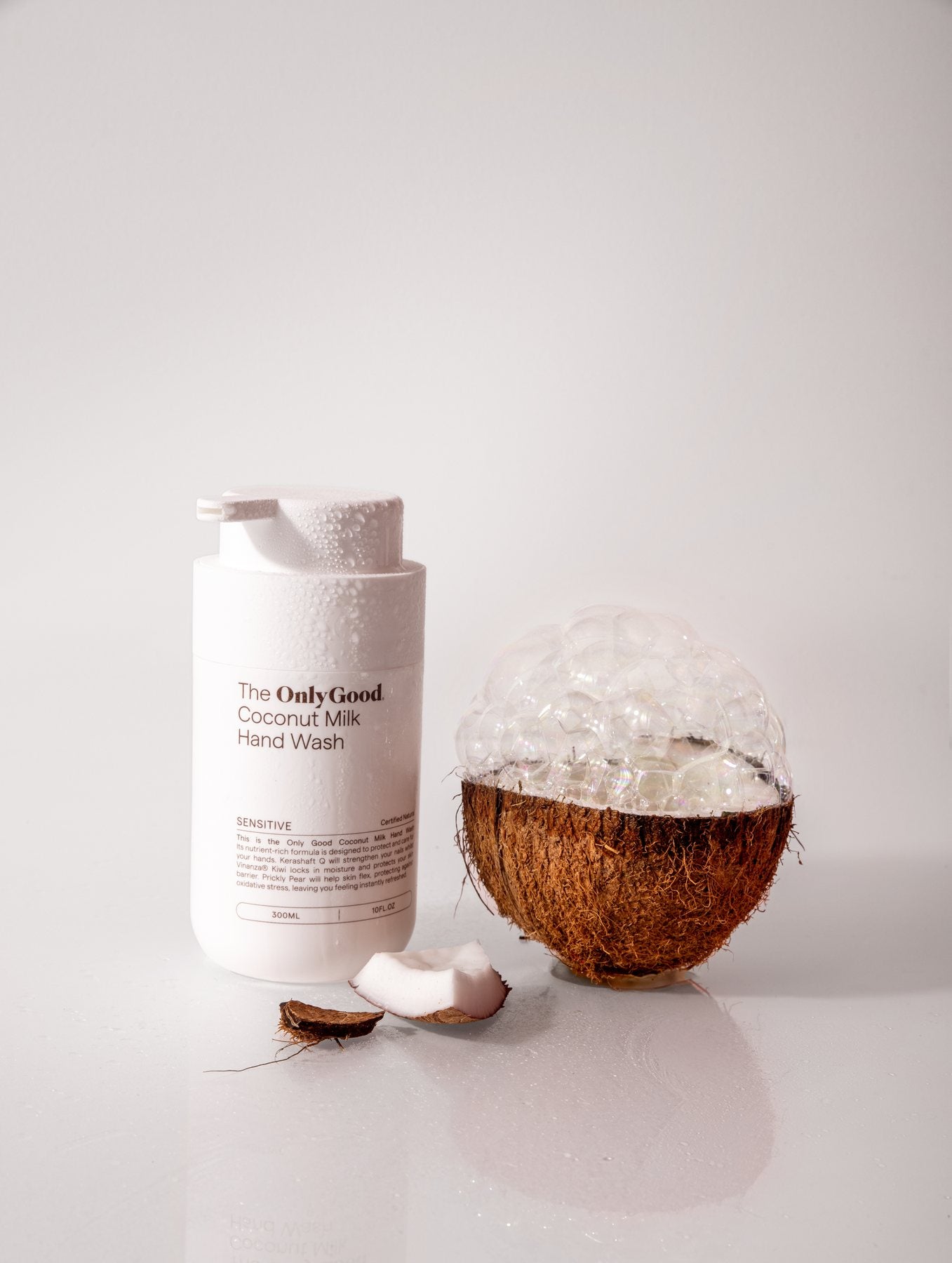 Only Good&reg; Coconut Milk Hand Wash beside a halved coconut crowned with foam.