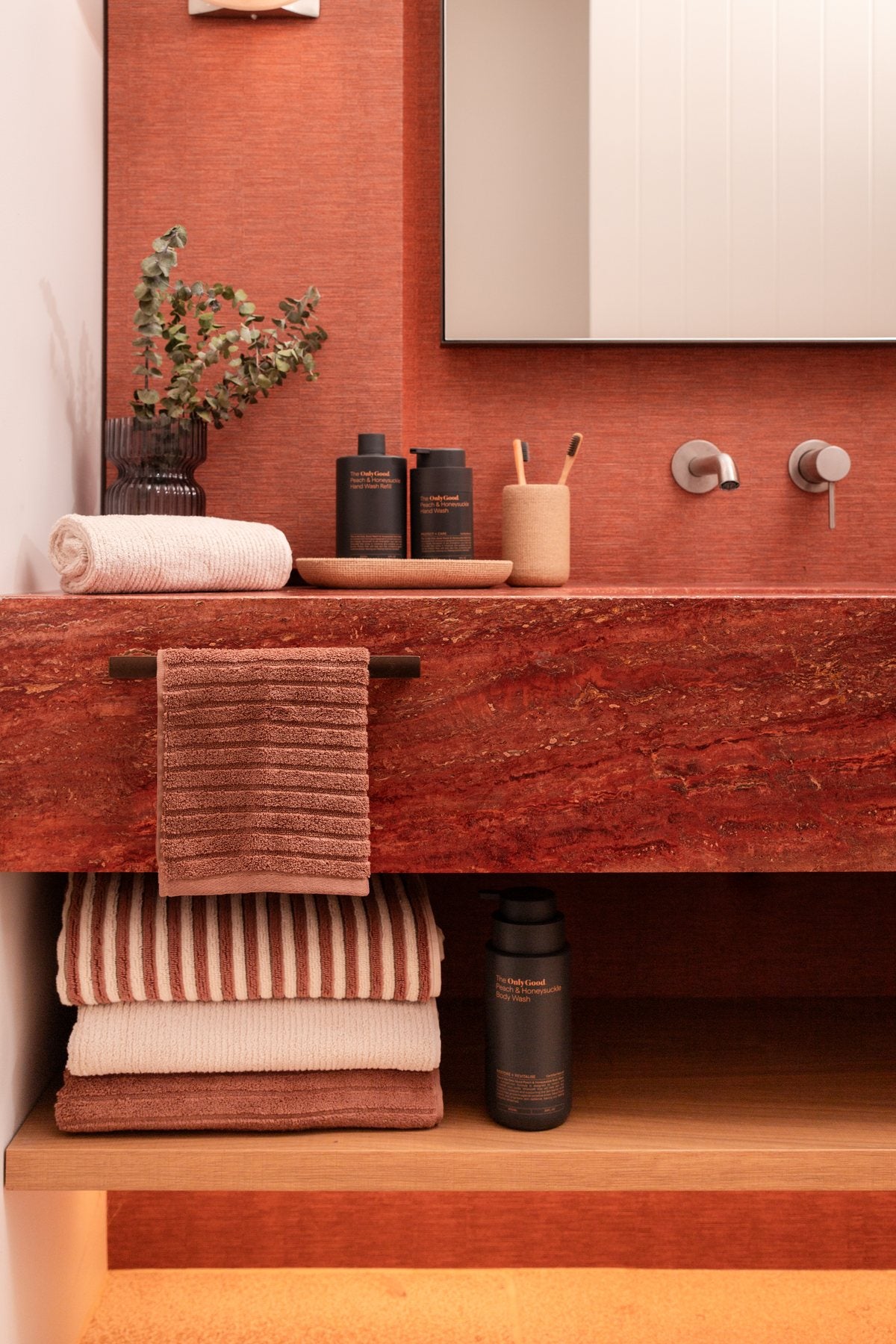 Only Good&reg; Peach & Honeysuckle on a red vanity with a mirror and towels.